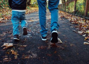 Adult and child's legs in jeans walking along a leafy path