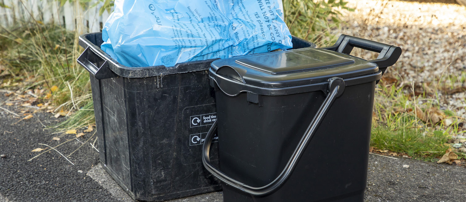 Black recycling box with blue recyling bag in it next to a black food waste caddy