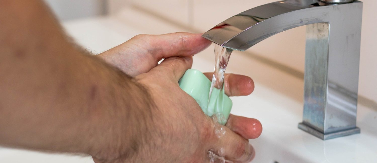 human hands being washed at a tap with bar of green soap