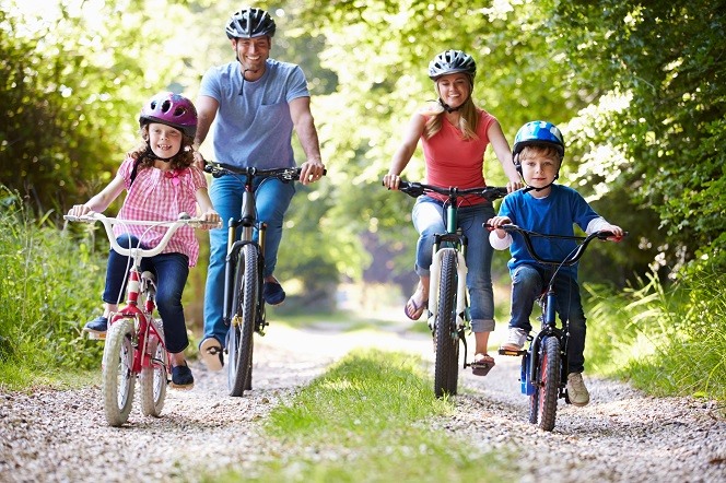 Man, woman, girl and boy cycling wearing helmets and smiling