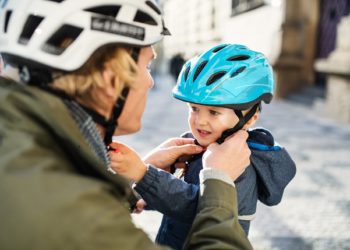 parent wearing cycle helmet putting a helmet on a child
