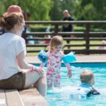 young children in paddling pool with lady sitting with feet in pool
