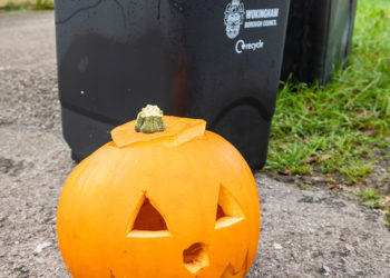 Carved pumpkin beside black food waste bins