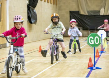 Young children on balance bikes in a sports hall