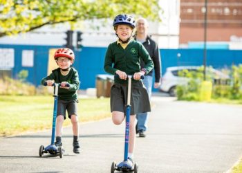 Young boy and girl in school uniform on scooters wearing cycle helmets