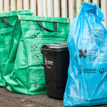 Two green recycling bags next to a black food waste caddy and a blue waste bag